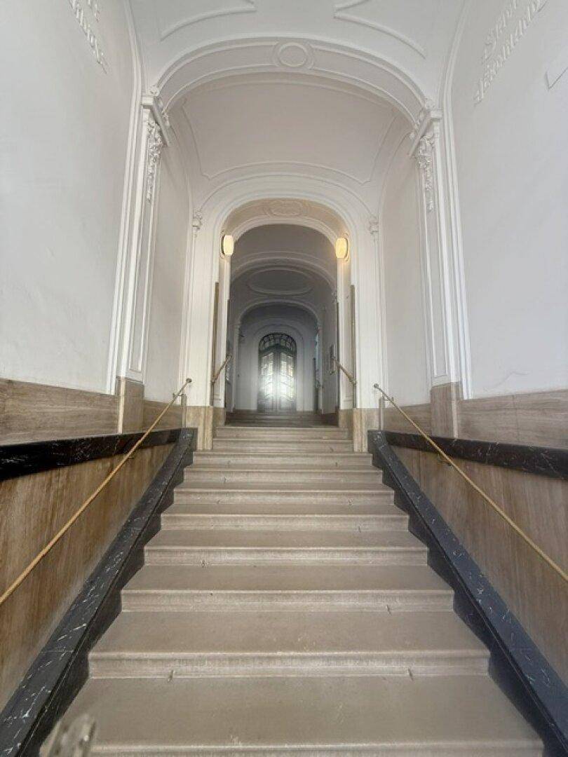 Historisches Treppenhaus mit Marmorstufen, verzierten Geländern und hohen Gewölbedecken.