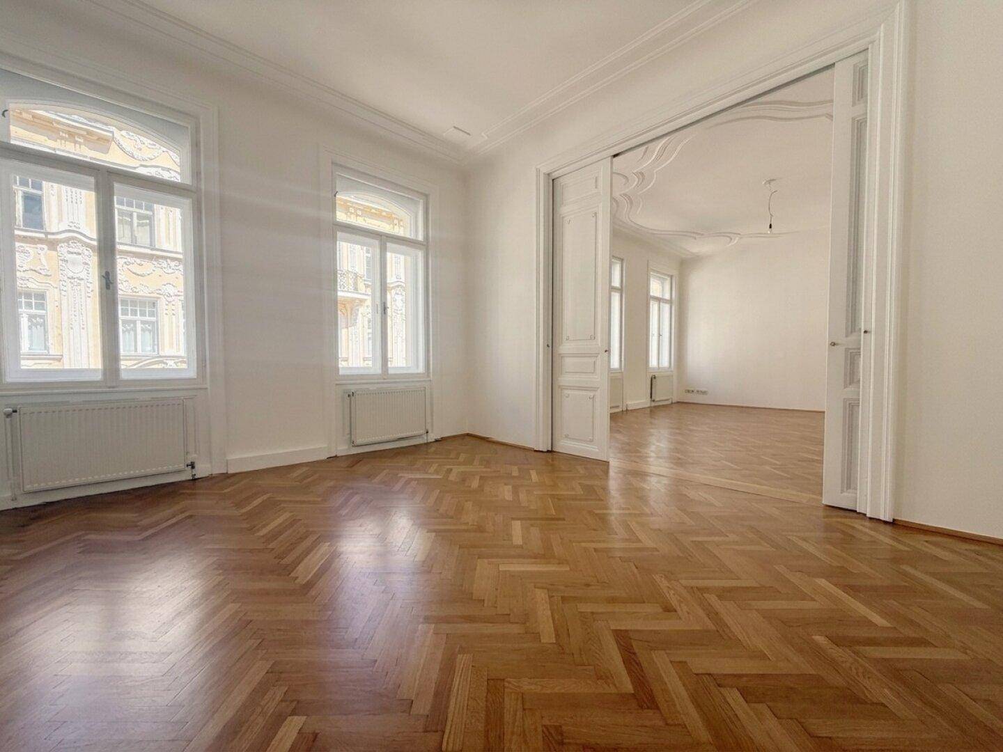 Klassisches Altbau-Zimmer mit glänzendem Fischgrätparkett, hohen Flügeltüren und viel Tageslicht.