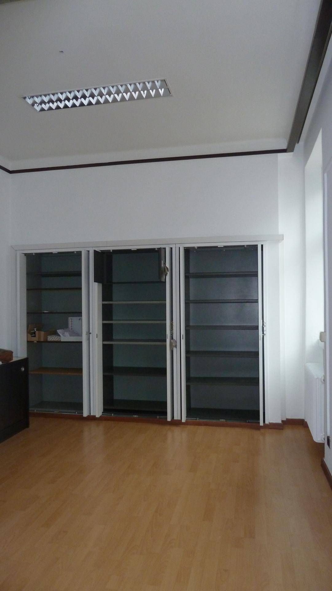 Büroraum mit hellem Holzfußboden und eingebauten Schränken für Stauraum.