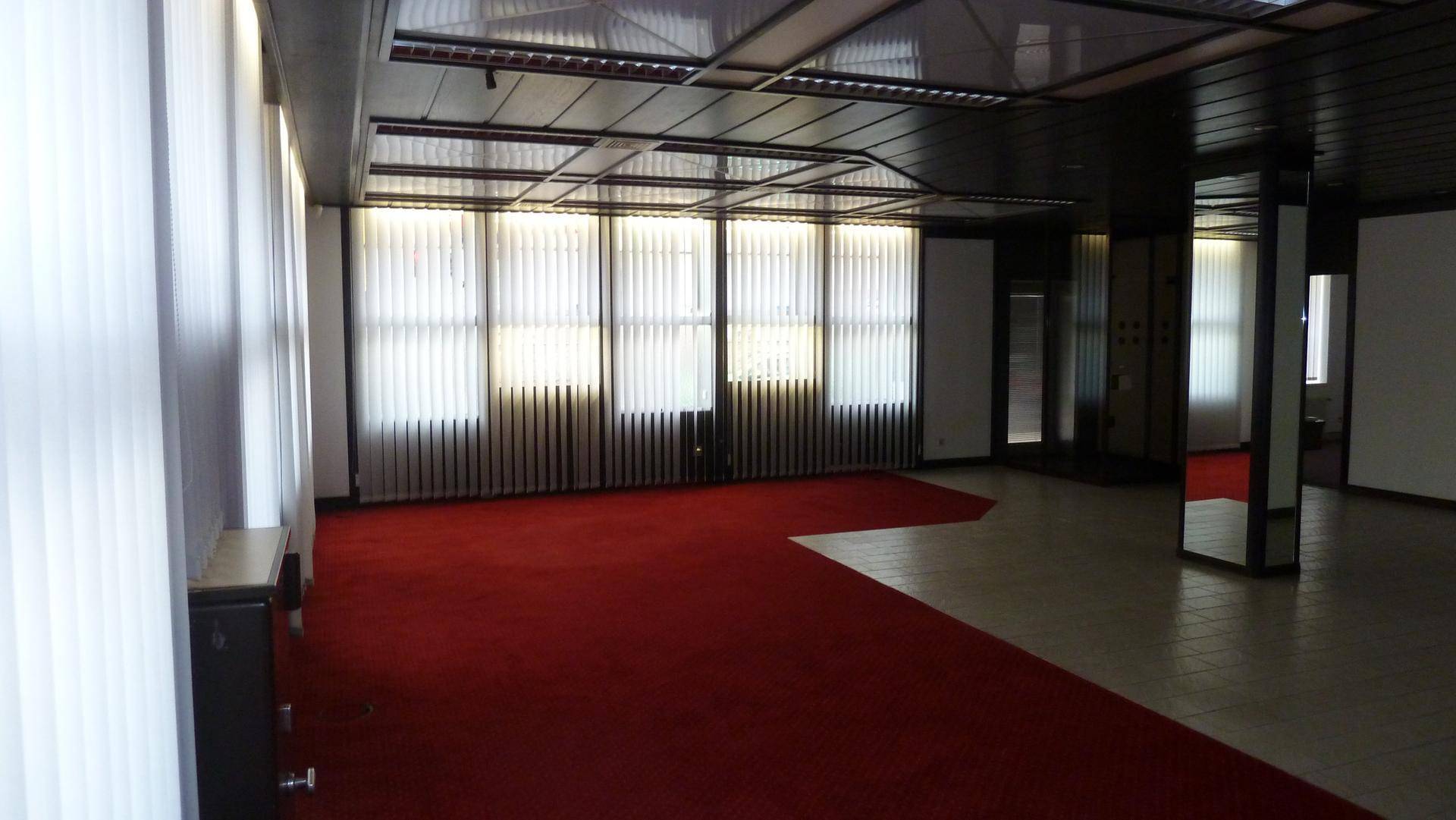 Großer Gewerberaum mit rotem Teppichboden, vertikalen Jalousien und Rasterdecke.