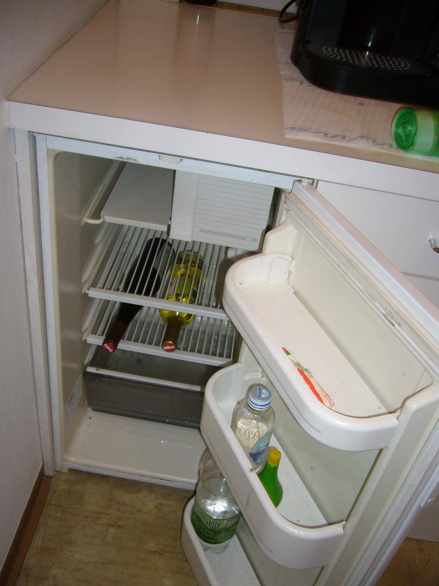 Offener kleiner Kühlschrank in einer Küchenzeile mit Getränken und Flaschen.