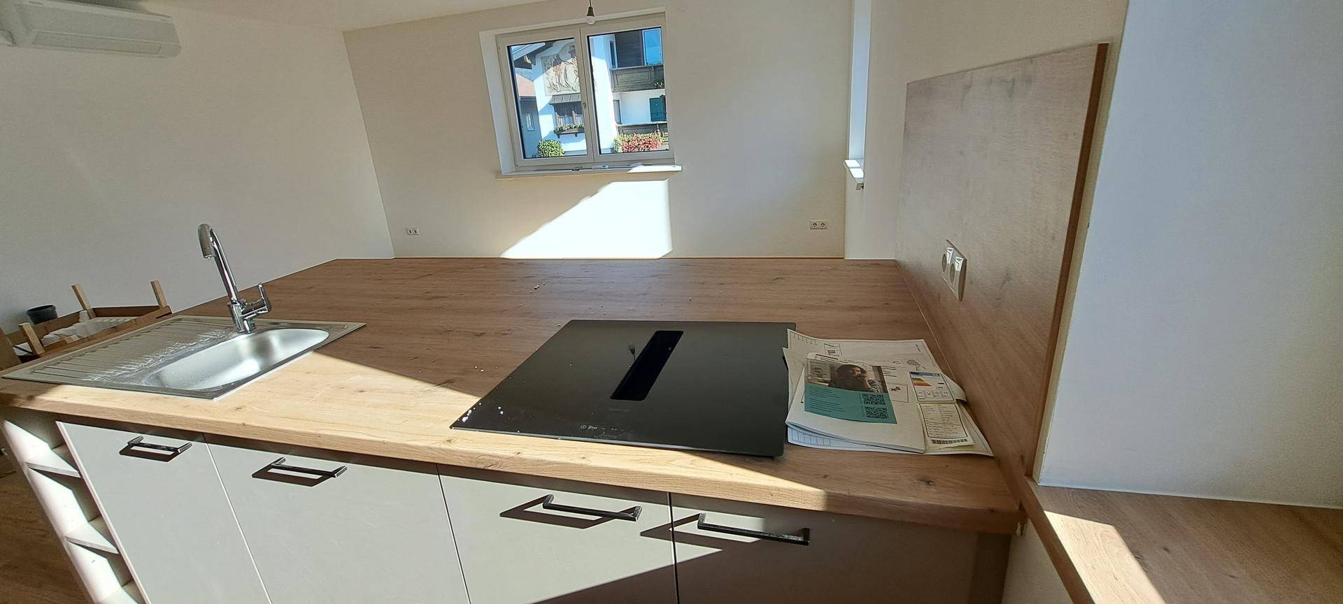 Nahaufnahme der Kücheninsel mit Spüle, Induktionskochfeld und Holzarbeitsplatte in sonnigem Licht.