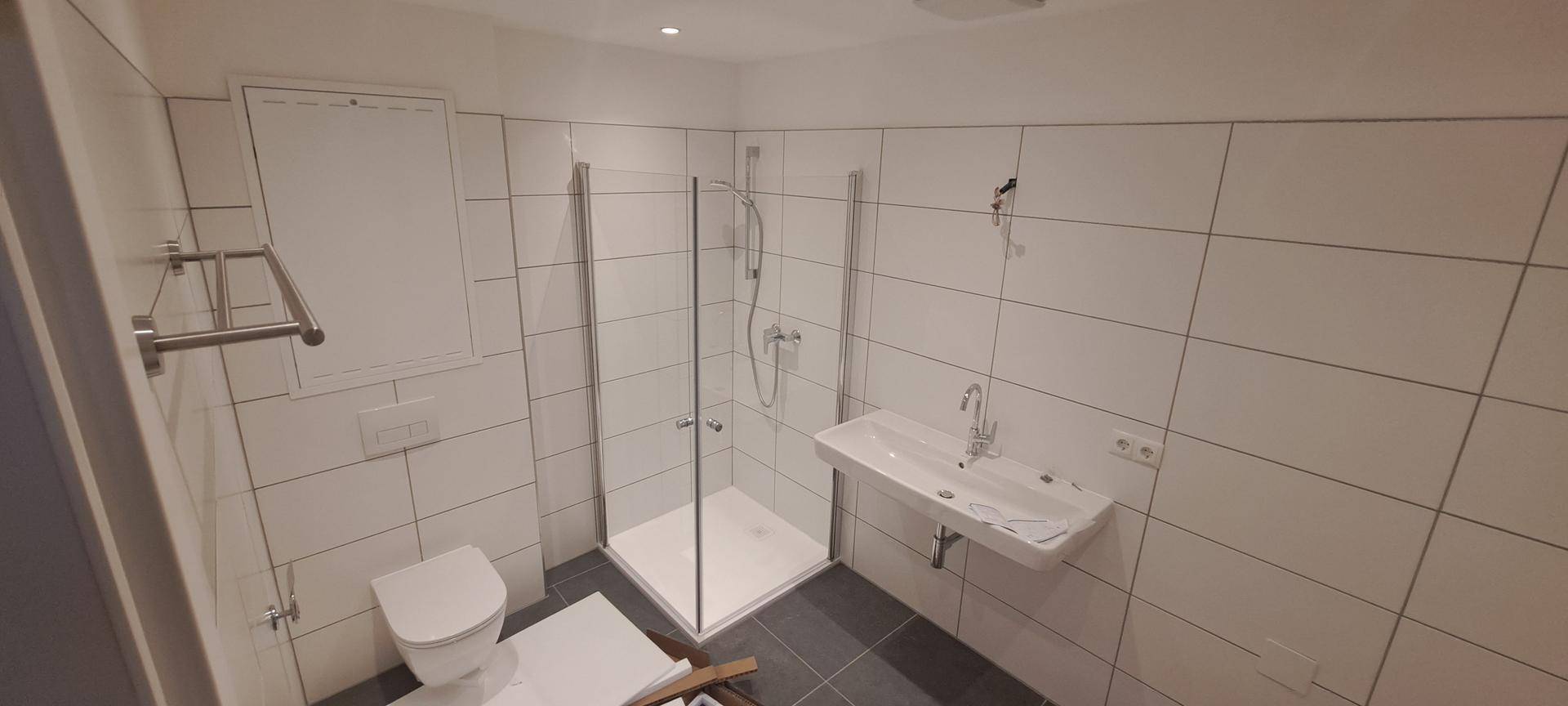 Helles Badezimmer mit weiß gefliesten Wänden, ebenerdiger Dusche und modernem Waschbecken.