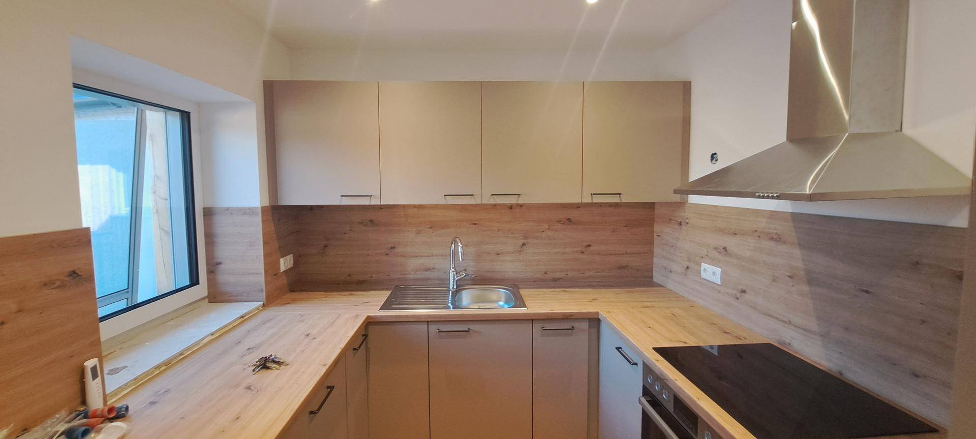 Detailansicht einer modernen Küche mit Holzoptik-Arbeitsplatten, Spüle und Induktionskochfeld.