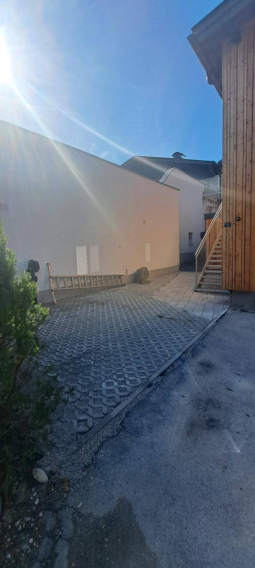 Außenbereich mit gepflasterter Fläche neben einem Gebäude mit Holzfassade unter blauem Himmel.
