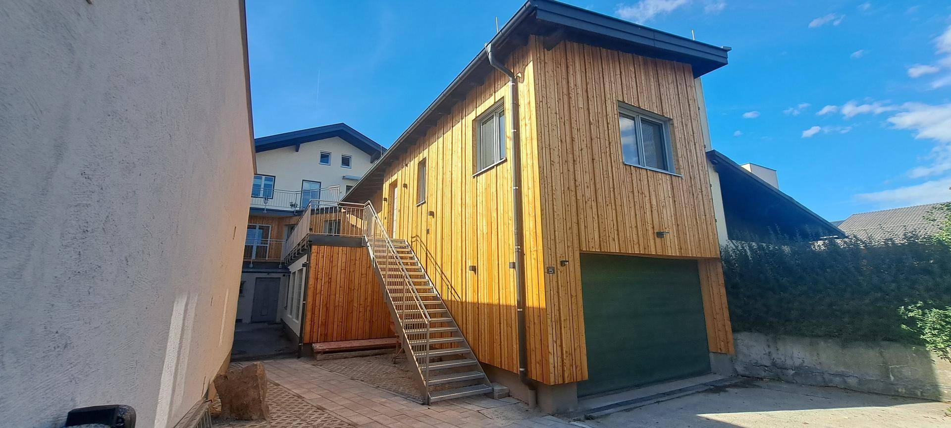 Modernes Gebäude mit Holzfassade und Außentreppe unter blauem Himmel.