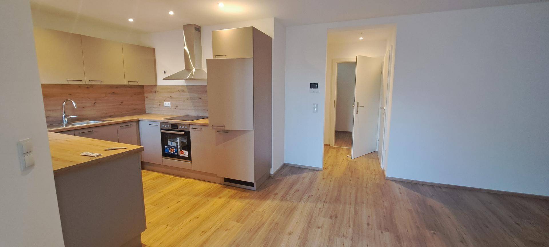 Moderne Einbauküche mit Holzoptik-Arbeitsplatten und hellem Laminatboden in einem offenen Wohnbereich.