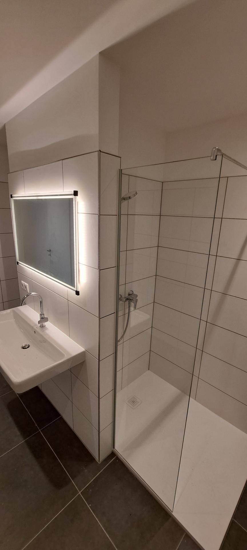 Helles Badezimmer mit moderner Duschkabine, Waschtisch und großformatigen Wandfliesen.