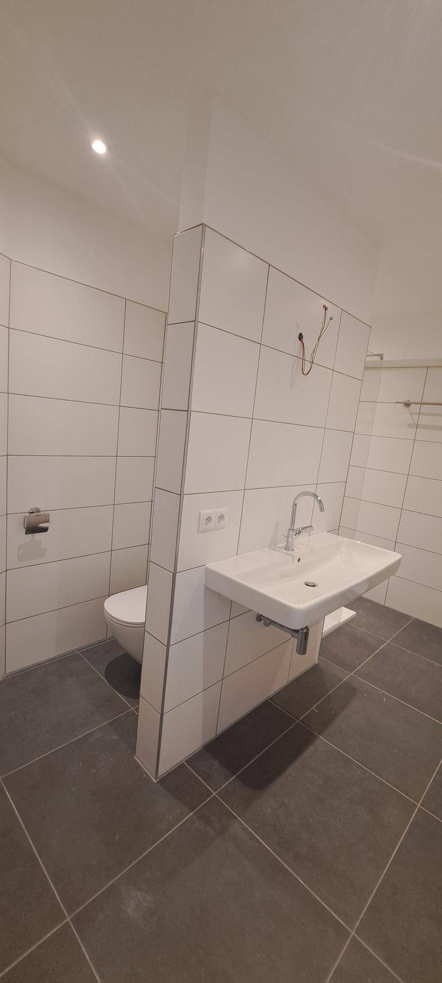 Helles Badezimmer mit modernem Waschbecken, Wand-WC und weißen Fliesen.