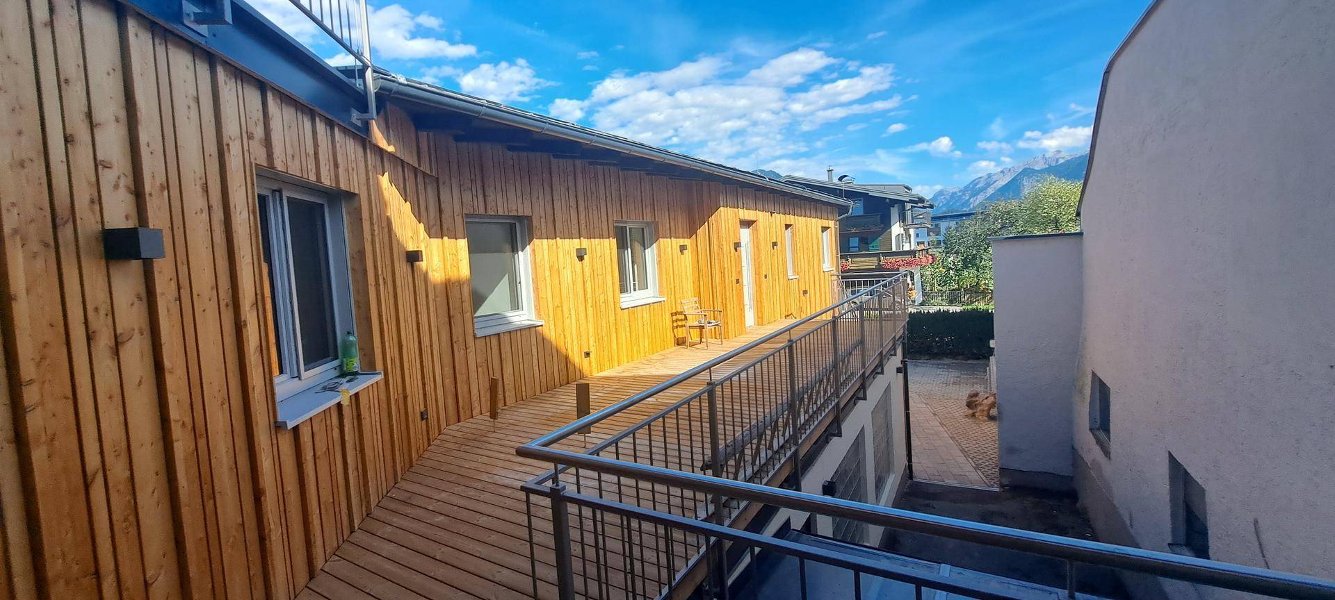 Langer Holzbalkon mit Metallgeländer entlang einer Holzfassade mit Blick auf die Berge.