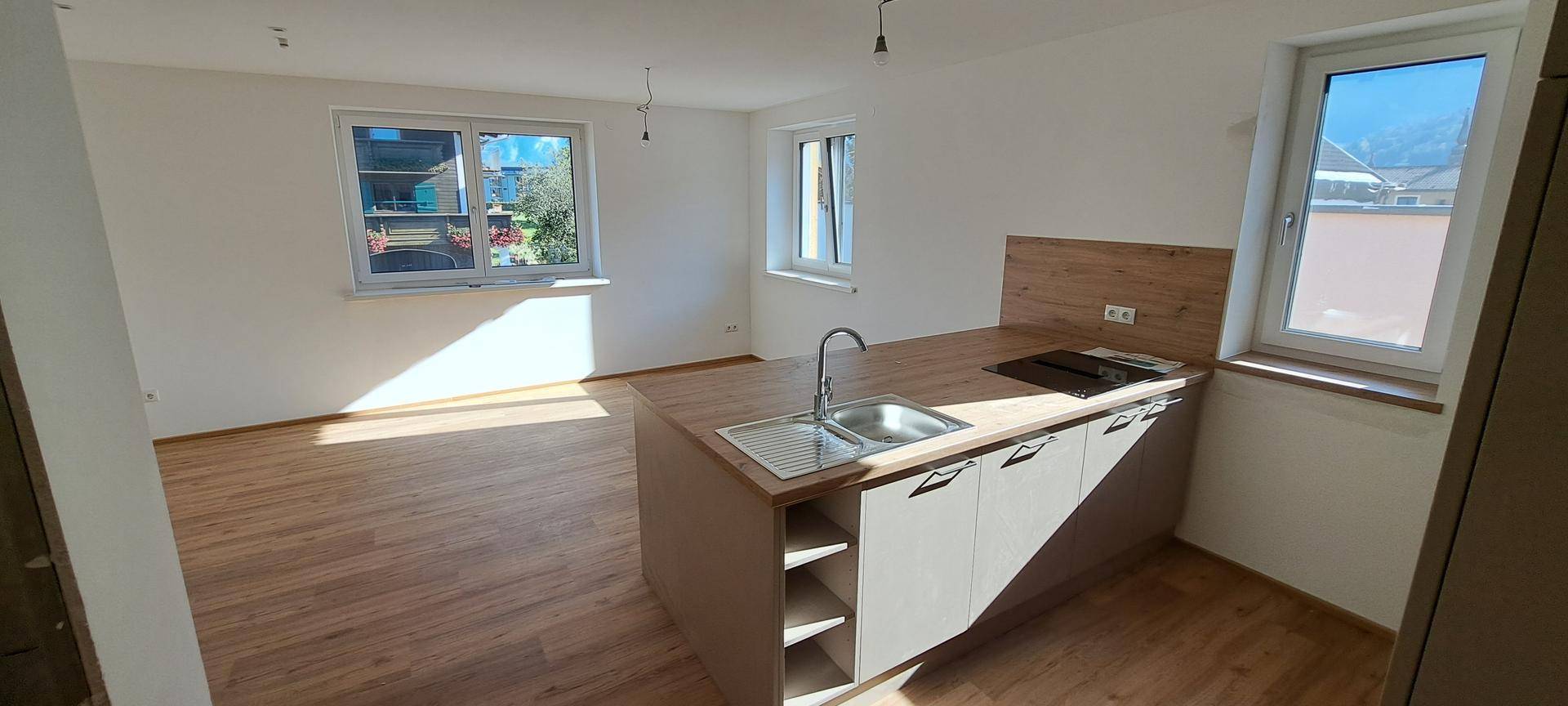 Helle Küche mit Kochinsel, Holzfußboden und großen Fenstern für viel Tageslicht im Wohnbereich.