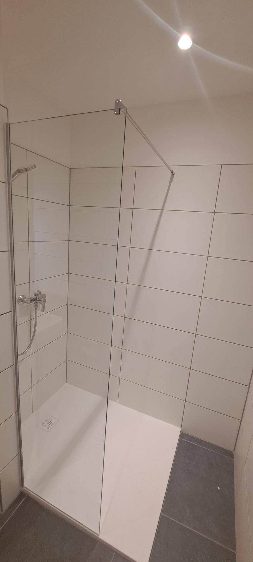 Modernes Badezimmer mit weiß gefliesten Wänden und einer geräumigen begehbaren Dusche.