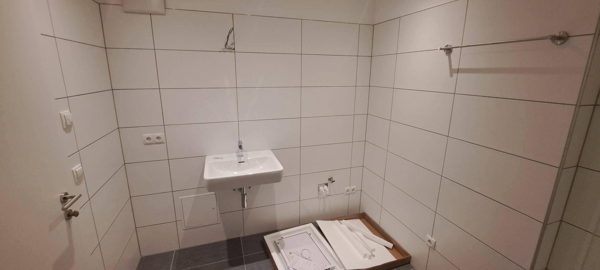 Helles Badezimmer mit weißen Fliesen und Waschbecken, bereit für die Endmontage der Armaturen.