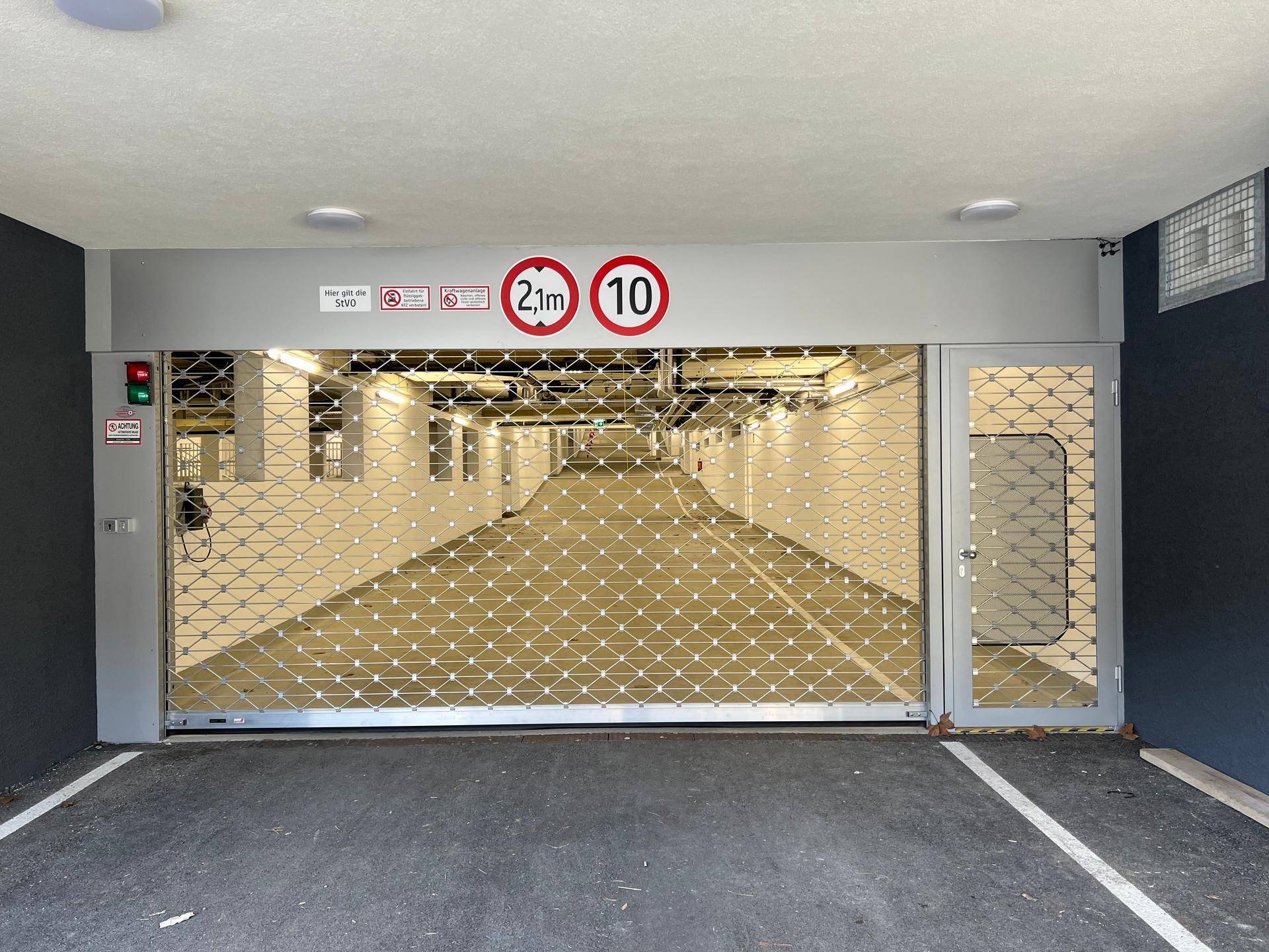 Einfahrt zur Tiefgarage mit Rolltor und Höhenbegrenzung, sicher und gut beleuchtet.