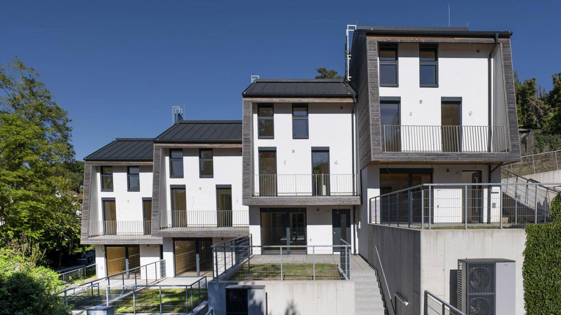 Neu gebaute Reihenhäuser mit weißer Fassade, Holzverkleidung und Balkonen unter blauem Himmel.