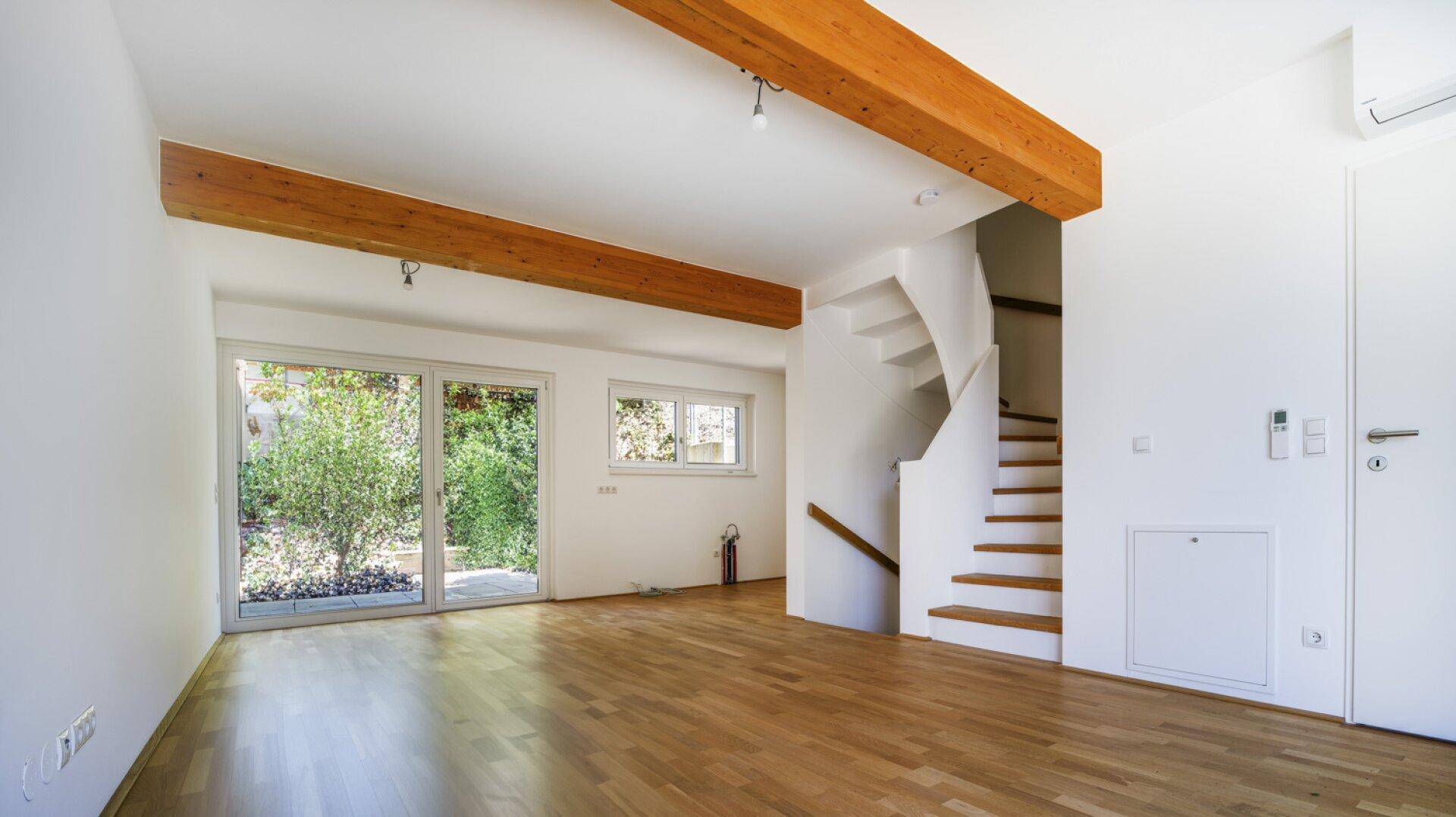 Geräumiges Wohnzimmer mit Holzbalken, Parkettboden und großen Fenstern zum Garten.