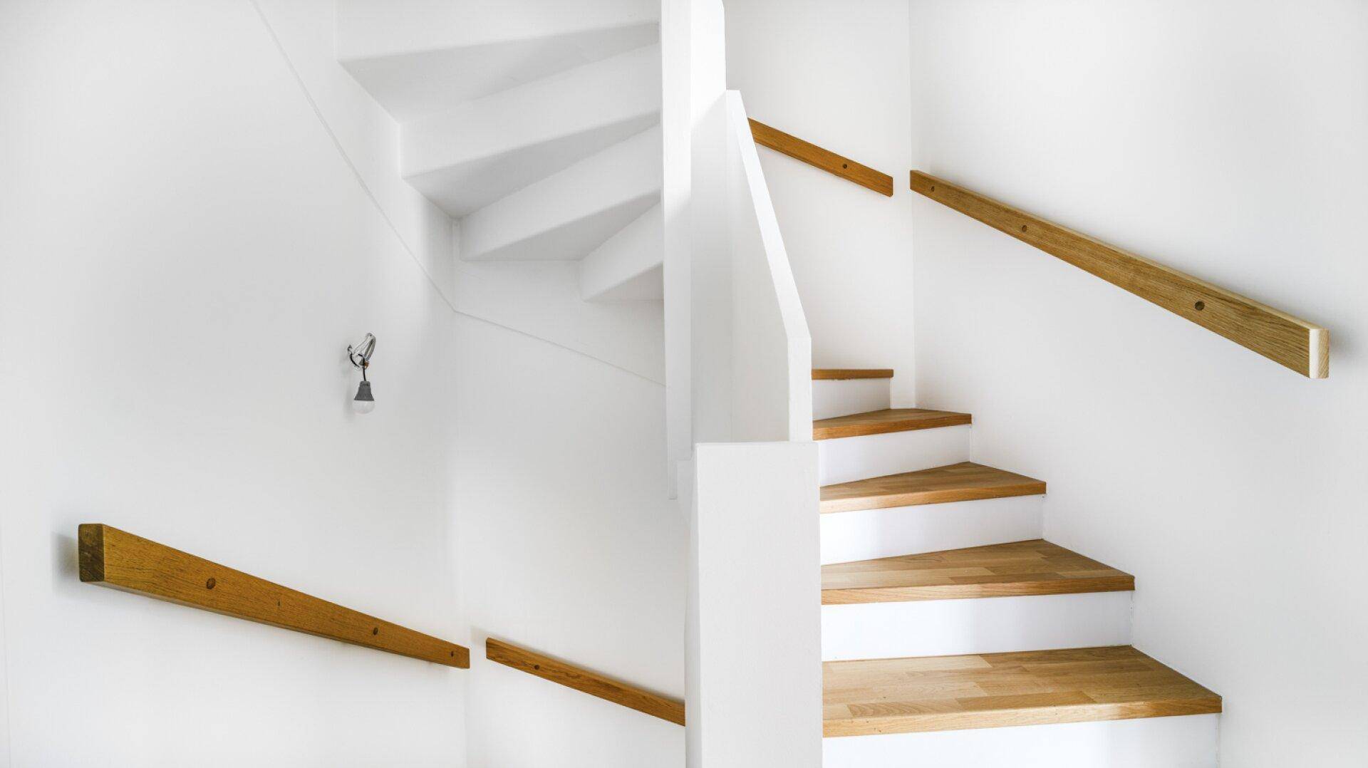 Moderne Holztreppe mit weißem Geländer und Handlauf in einem hellen Treppenhaus.