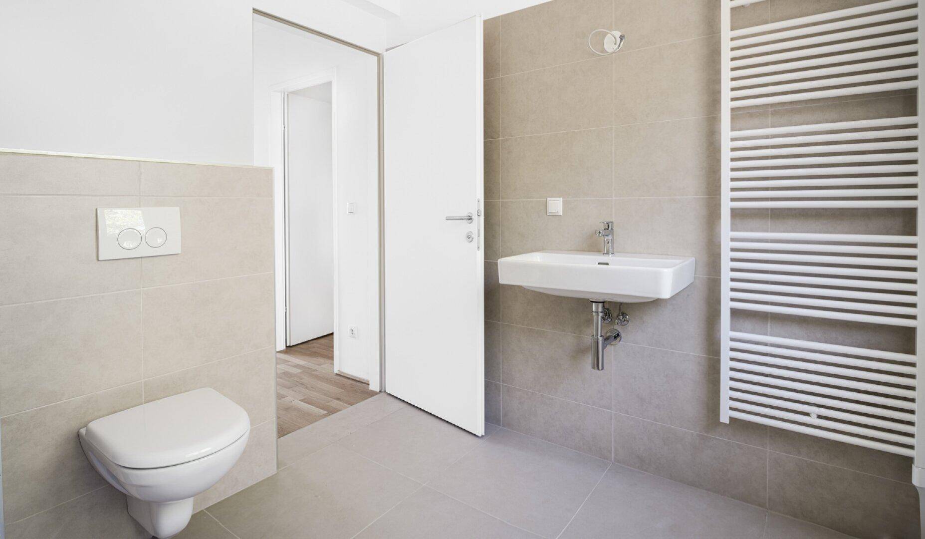 Helles Badezimmer mit wandhängendem WC, Waschbecken und beheiztem Handtuchhalter.