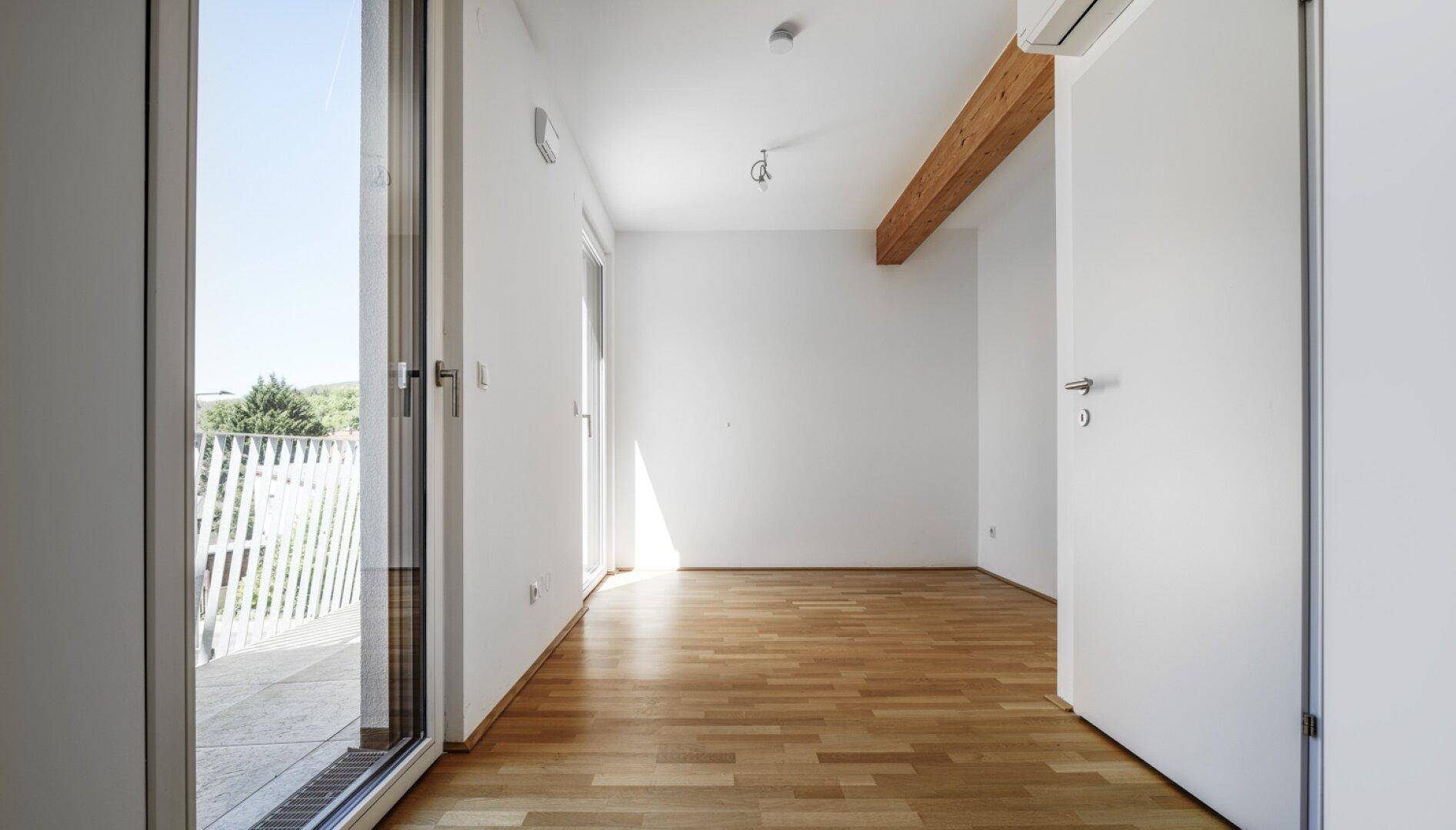 Helles Schlafzimmer mit Parkettboden, Holzbalken und Zugang zu einem Balkon.