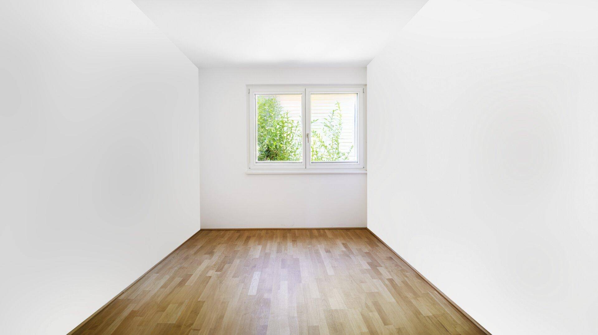 Leeres Zimmer mit Parkettboden und Fenster, das viel natürliches Licht hereinlässt.