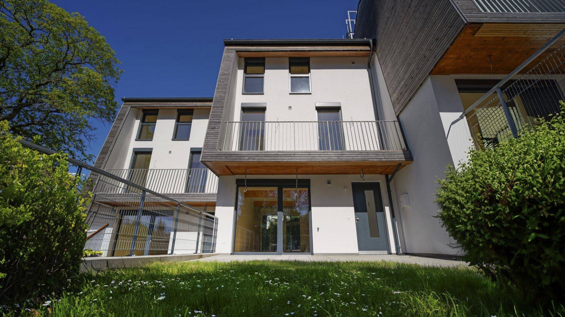 Moderne Reihenhäuser mit weißer Fassade, Holzverkleidung und kleinen Gärten.