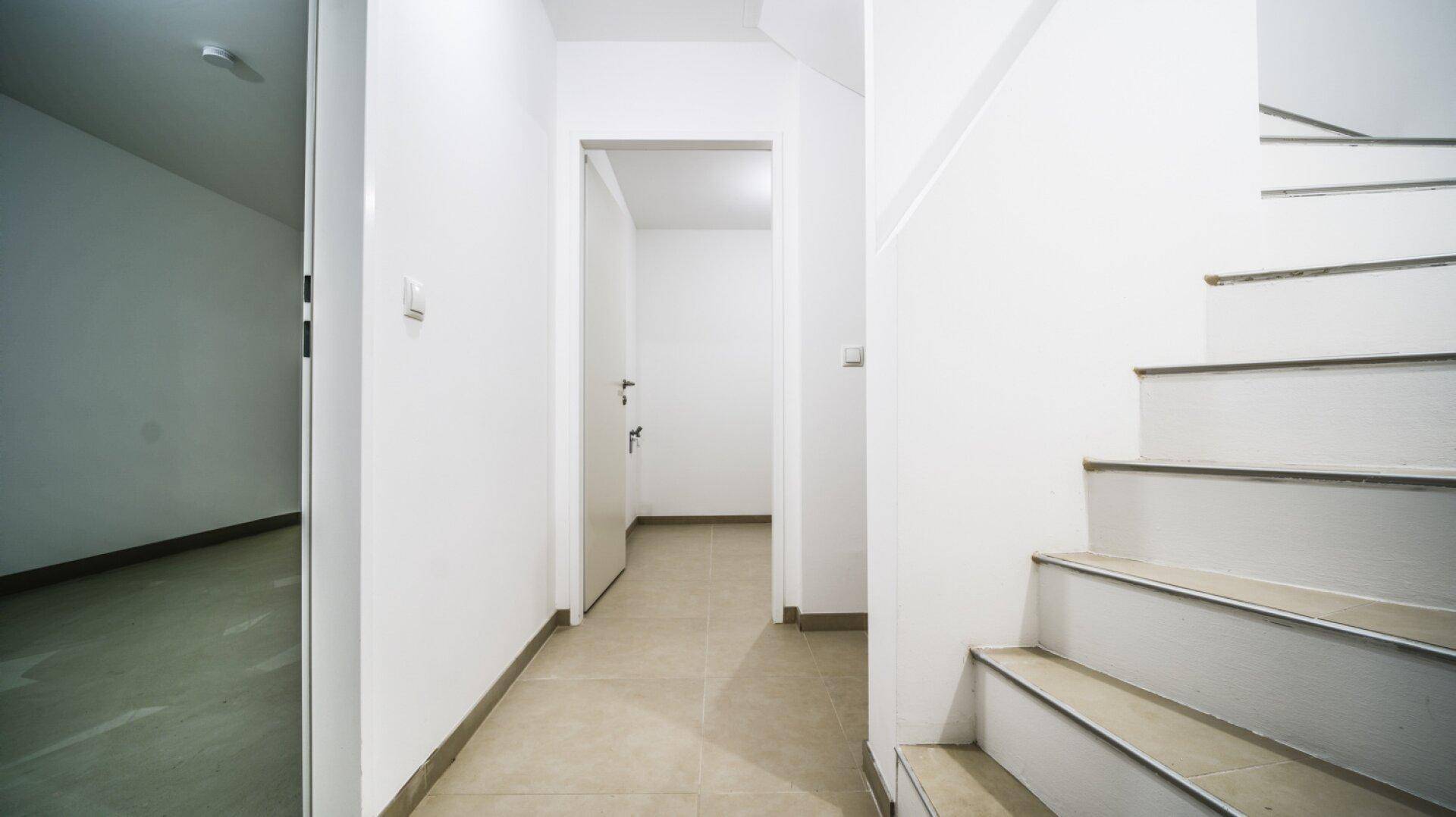 Heller Flur mit Fliesenboden und Treppe, der zu verschiedenen Räumen führt.