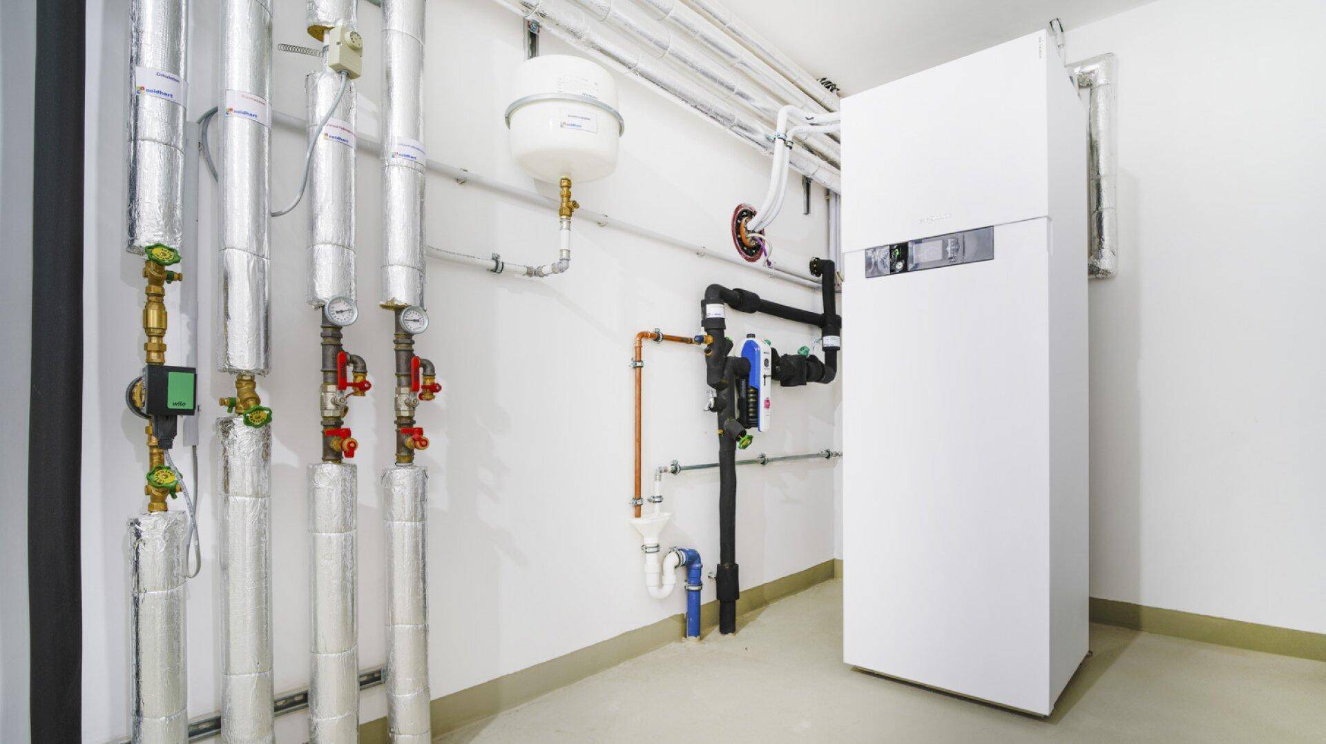 Moderner Heizungsraum mit Wärmepumpe und zahlreichen Installationen in einem Neubau.