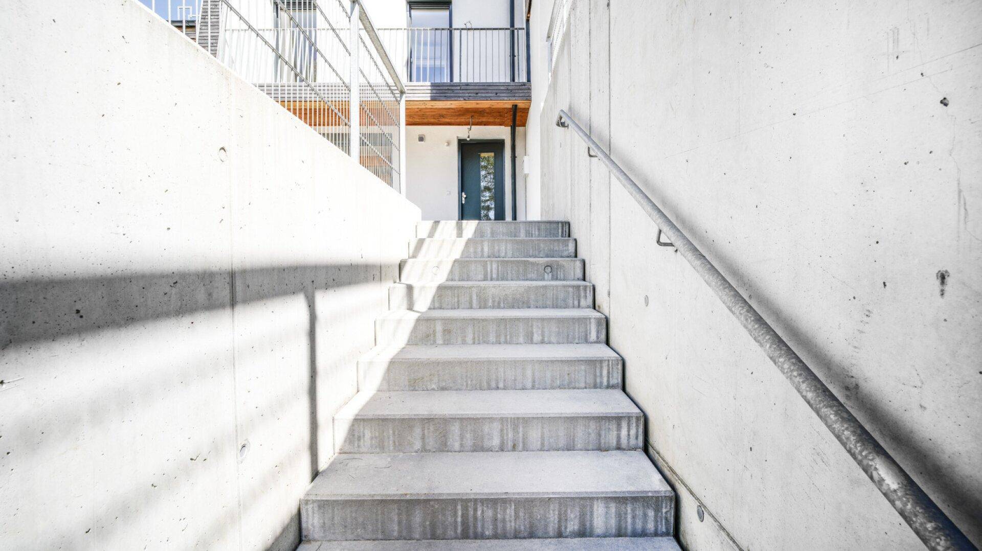 Außentreppe aus Beton mit Handlauf führt zum Eingangsbereich eines modernen Gebäudes.