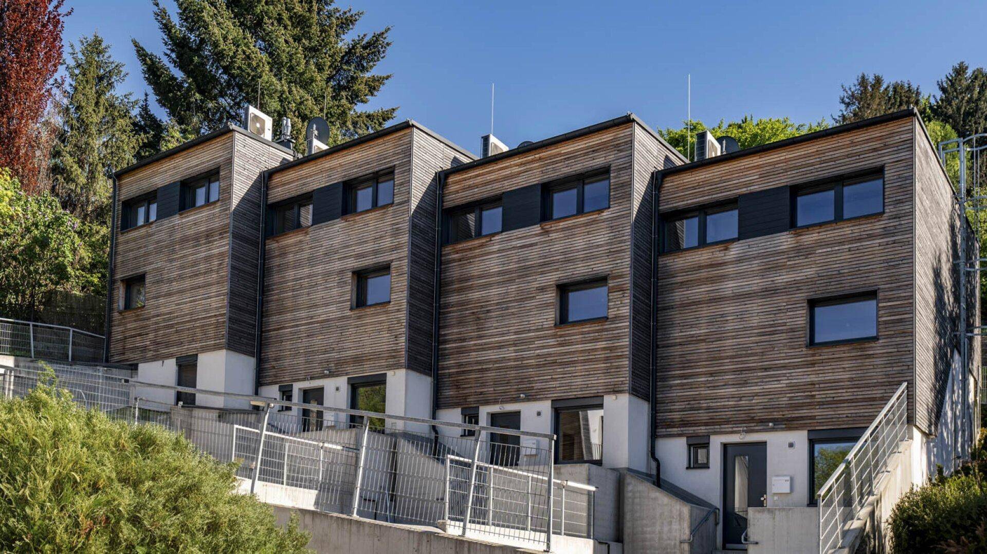 Moderne Reihenhäuser mit Holzverkleidung und großen Fenstern in einer ruhigen Wohngegend.
