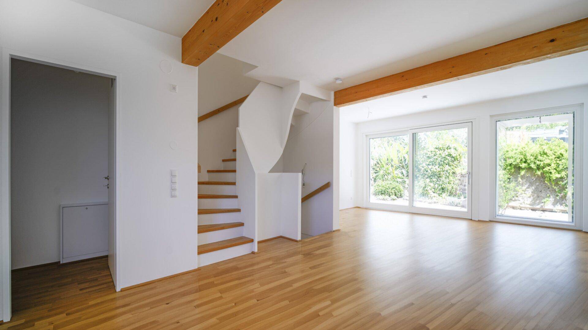 Heller Wohnbereich mit Holzparkettboden, offener Treppe und großen Fenstern zum Garten.