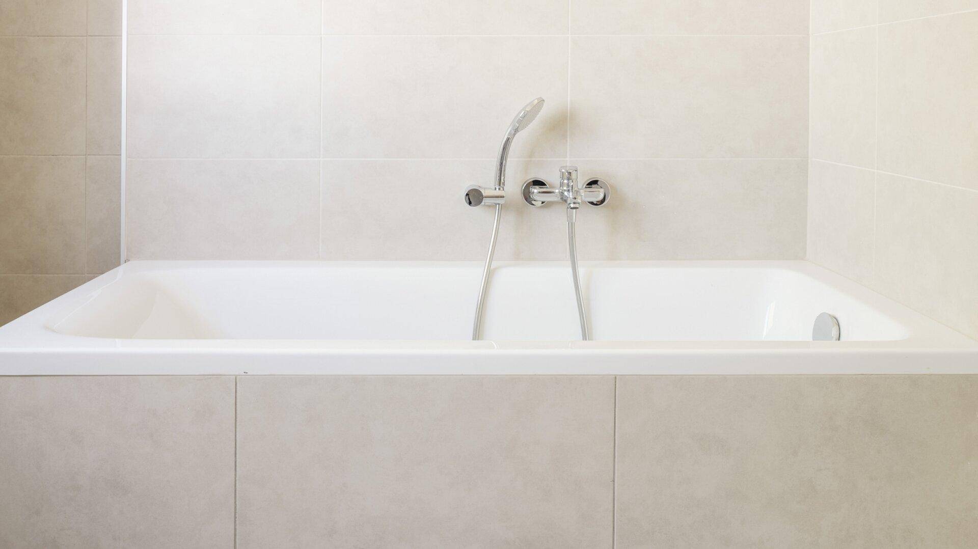 Eingebaute Badewanne mit beigefarbenen Fliesen und Duscharmatur in einem modernen Badezimmer.