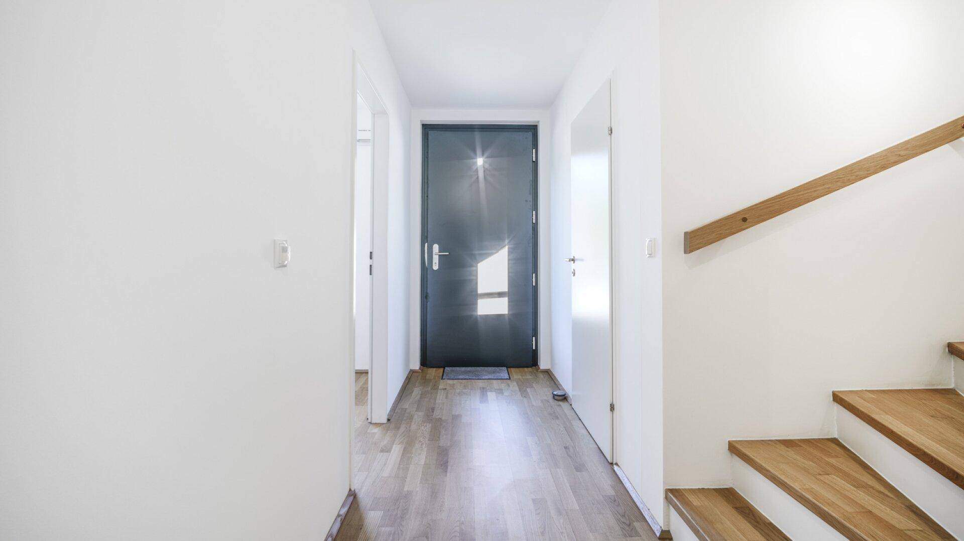 Heller Eingangsbereich mit Holzboden und einer modernen dunklen Eingangstür.