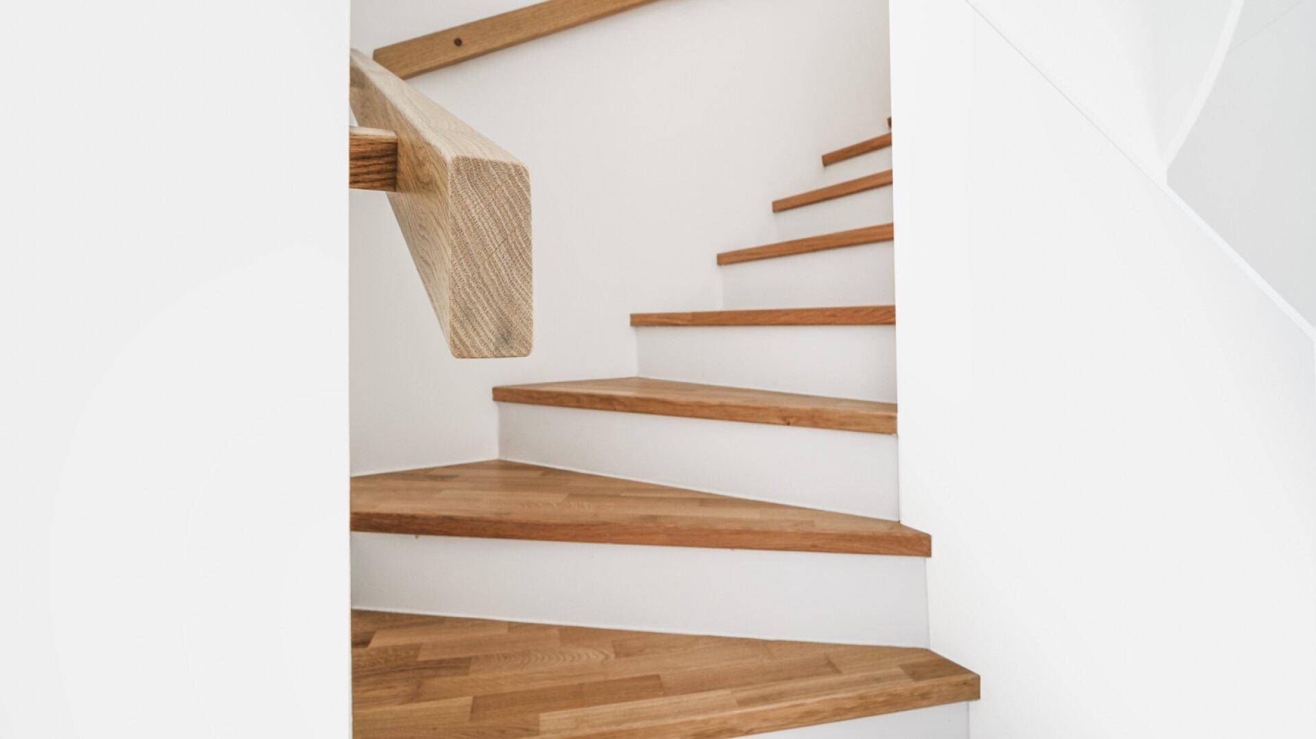 Detailansicht einer modernen Holztreppe mit hellem Holzgeländer und weißen Wänden.