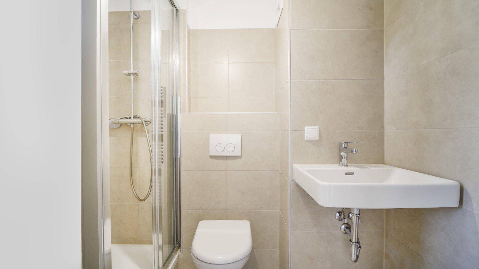 Modernes Badezimmer mit Duschkabine, wandhängendem WC und Waschbecken, gefliest in Beige.