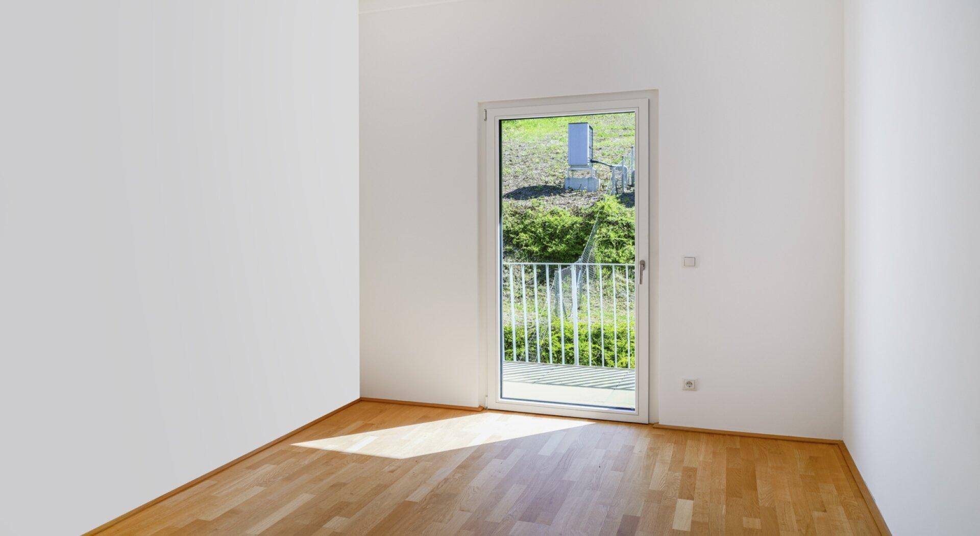 Helles Zimmer mit Parkettboden und Zugang zu einem französischen Balkon mit Blick ins Grüne.