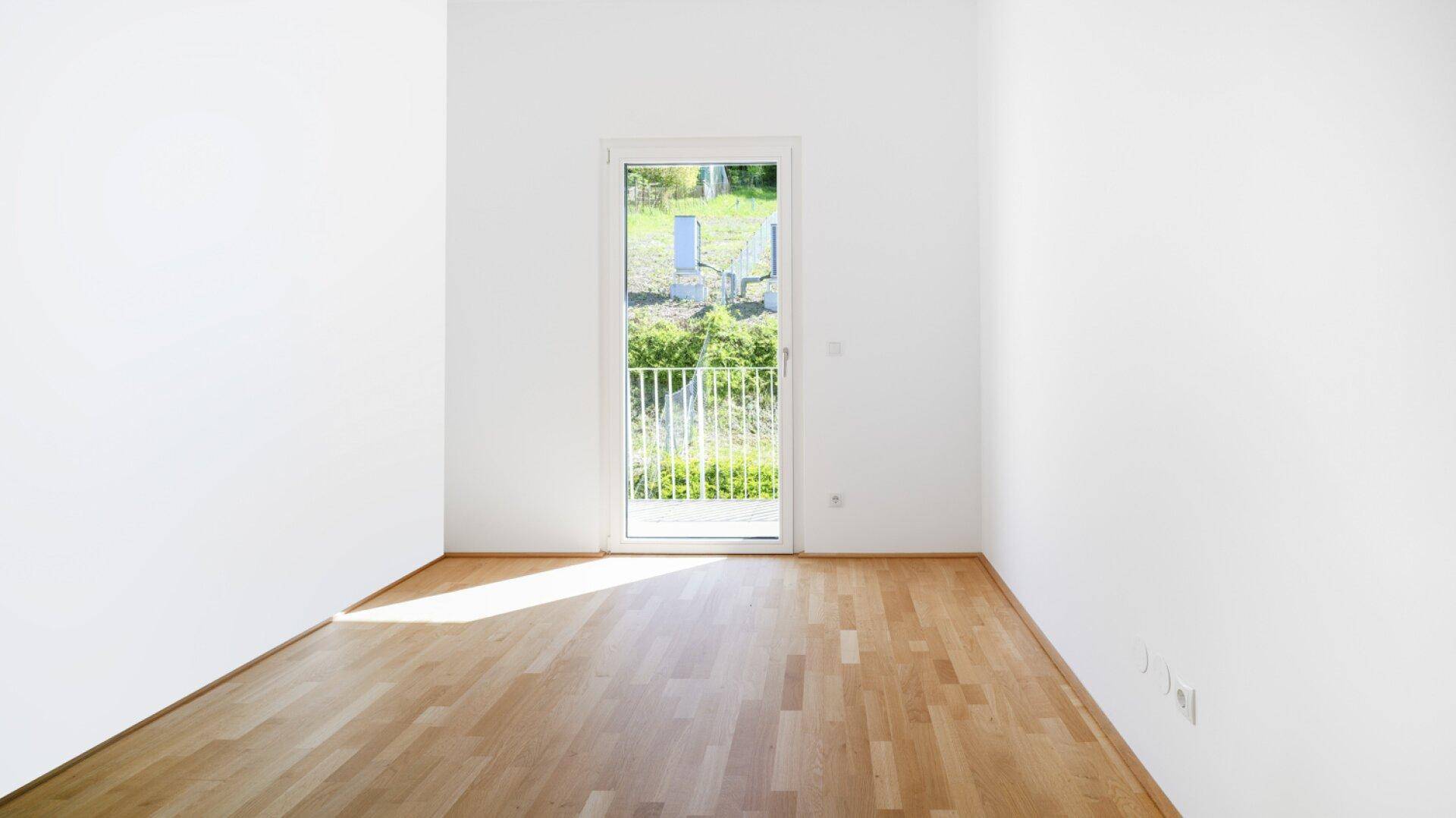 Lichtdurchflutetes Zimmer mit Parkettboden und Zugang zu einem kleinen Balkon mit Aussicht.