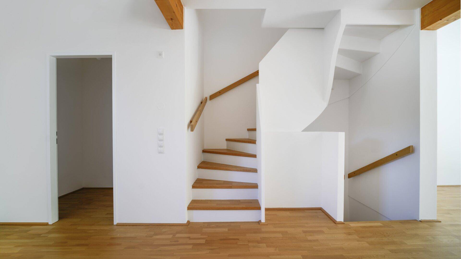 Moderne Holztreppe mit weißem Geländer in einem hellen Eingangsbereich.