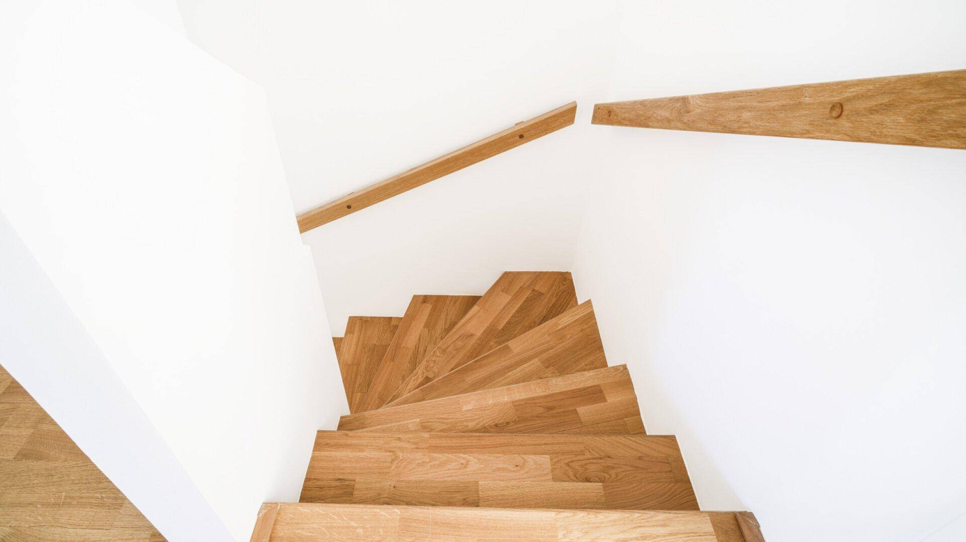 Blick von oben auf eine elegante Holztreppe mit weißen Setzstufen und Holzgeländer.