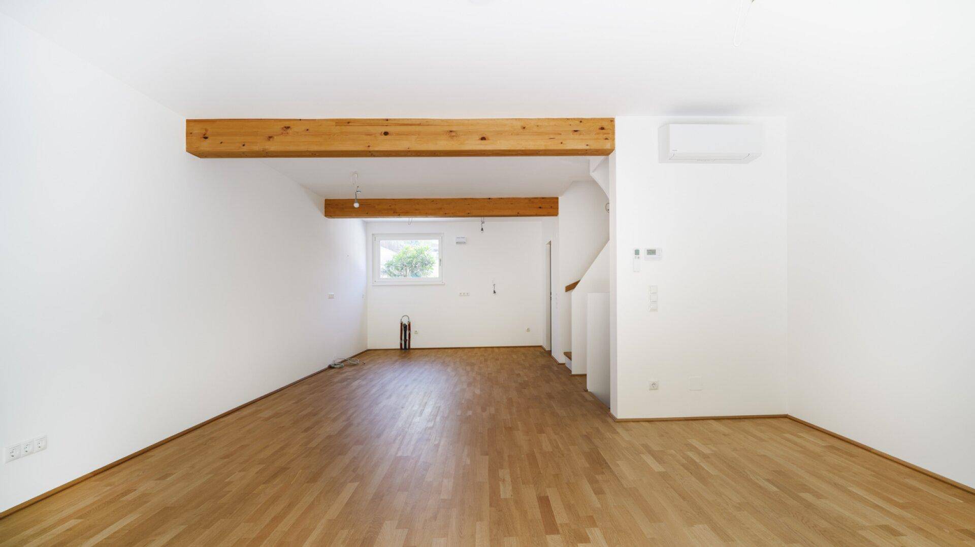 Geräumiger Wohnbereich mit Holzbalken, Parkettboden und Klimaanlage, bereit zum Einrichten.