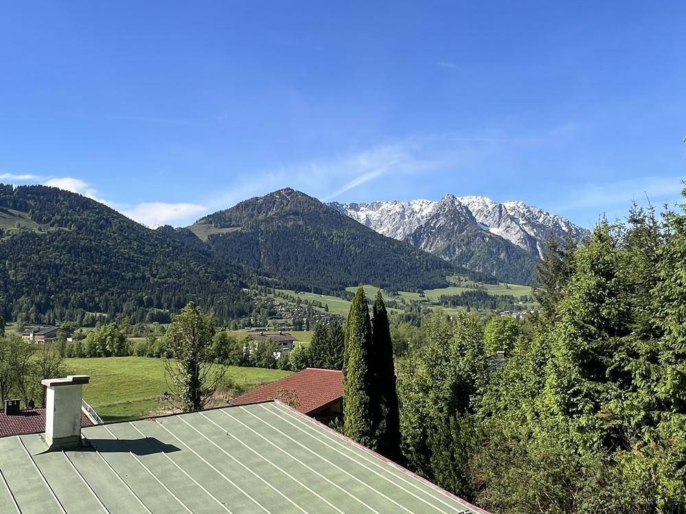 Atemberaubender Panoramablick auf schneebedeckte Berge und grüne Täler unter blauem Himmel.