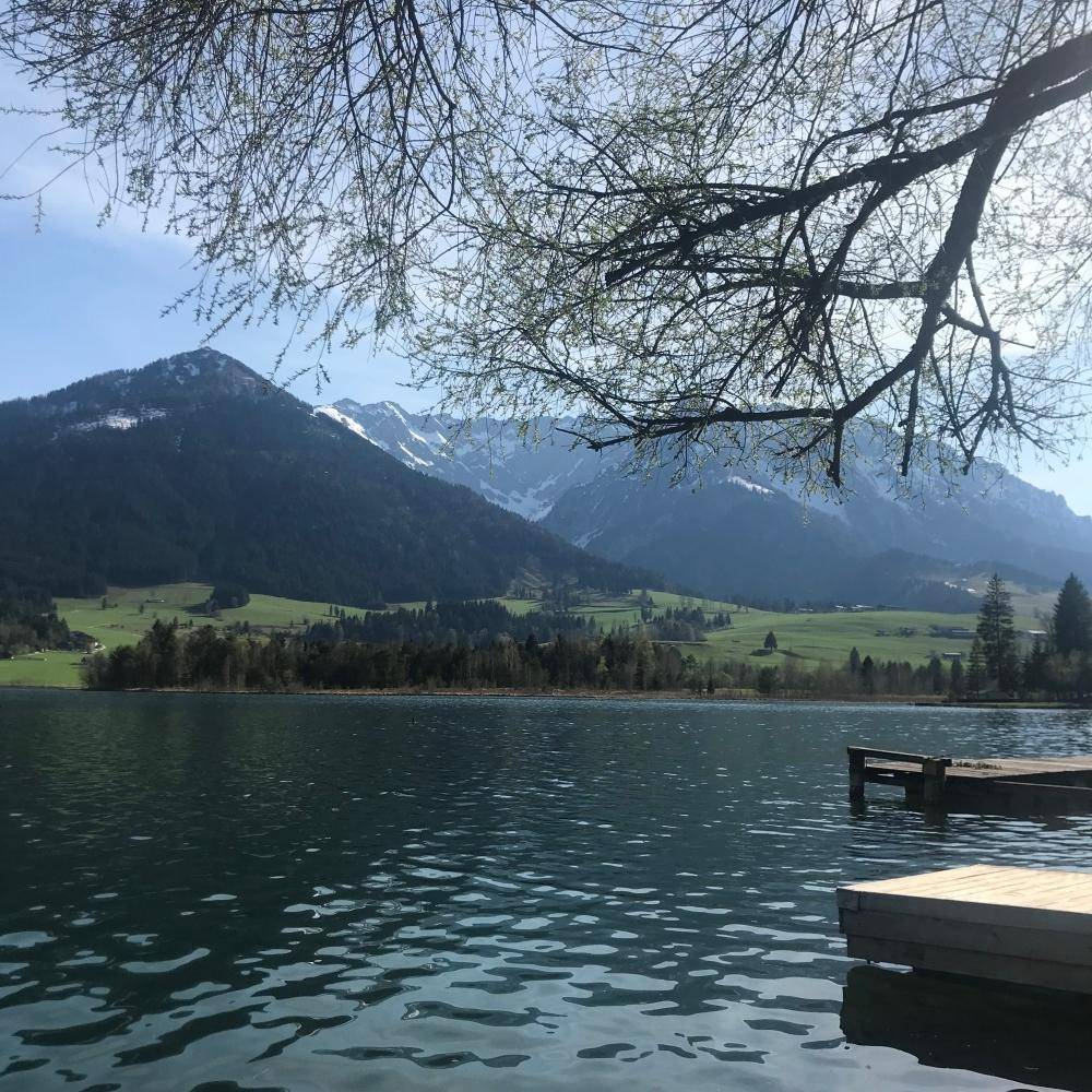 Idyllischer See mit majestätischen Bergen im Hintergrund unter blauem Himmel.