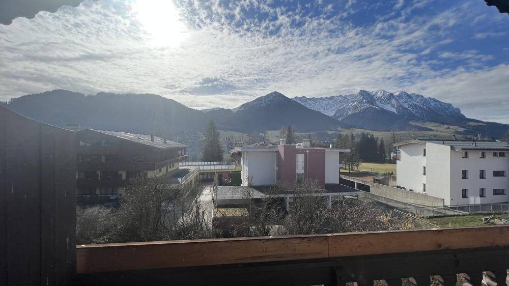 Weitblick über die Stadt und schneebedeckte Berge von einem sonnigen Balkon aus.