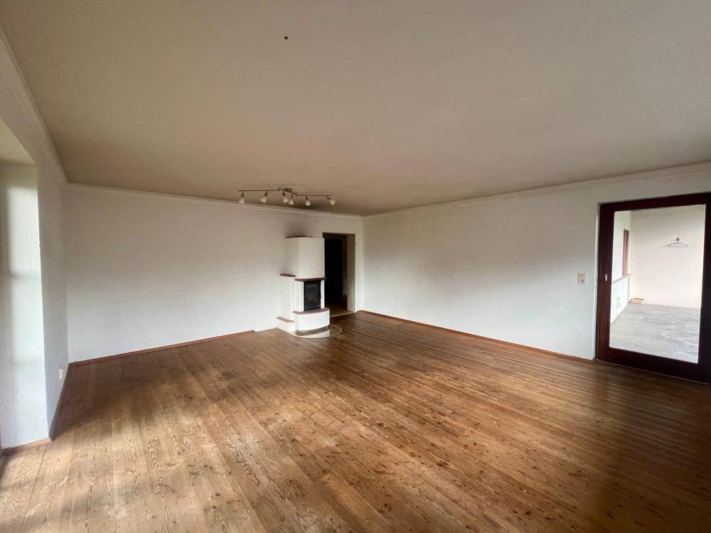 Geräumiges Wohnzimmer mit Holzboden und einem traditionellen Kachelofen als Blickfang.