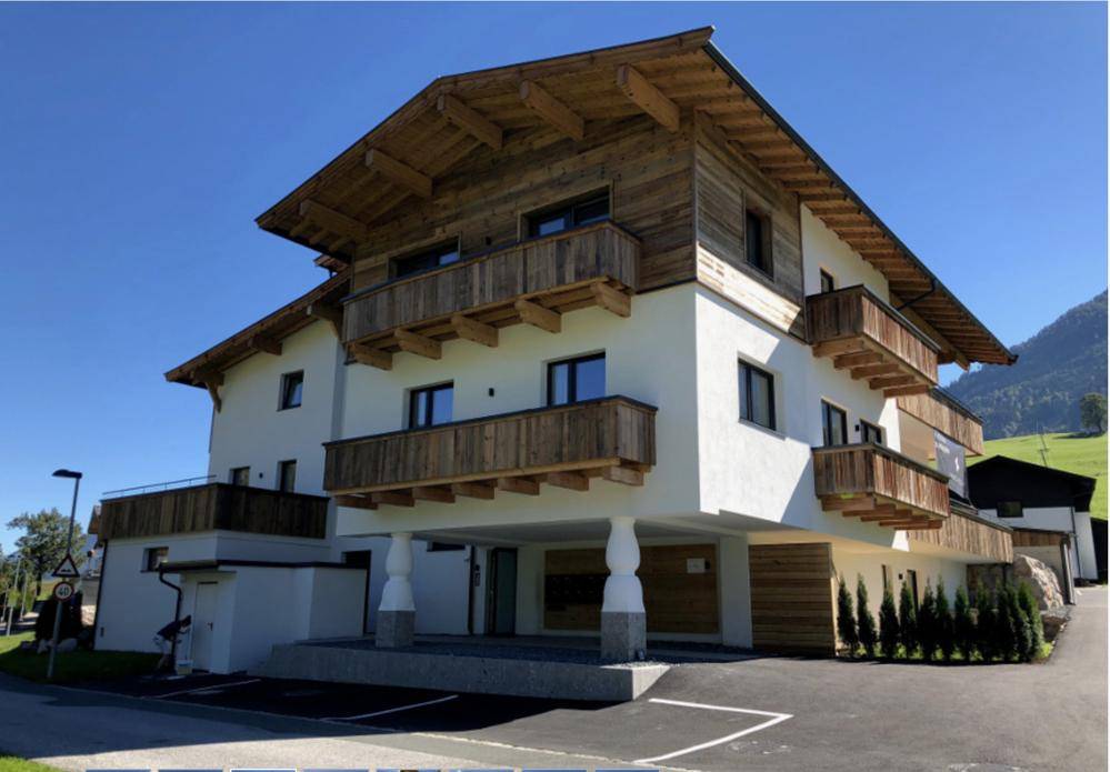 Neubau im traditionellen alpinen Stil mit Holzverkleidung und mehreren Balkonen, umgeben von Natur.