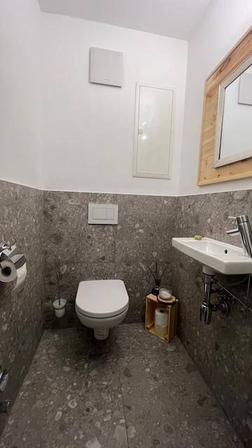Separates WC mit Wand-WC, kleinem Waschbecken und modernem Fliesenboden.