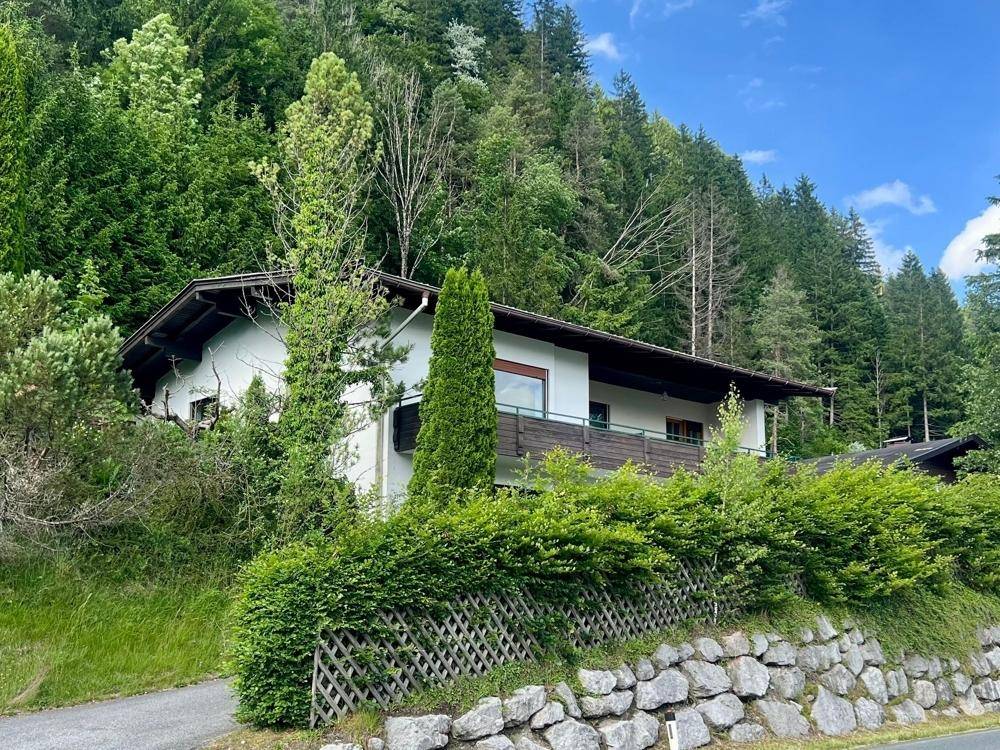 Seitliche Ansicht des Hauses mit Balkon und üppiger Vegetation im alpinen Stil.