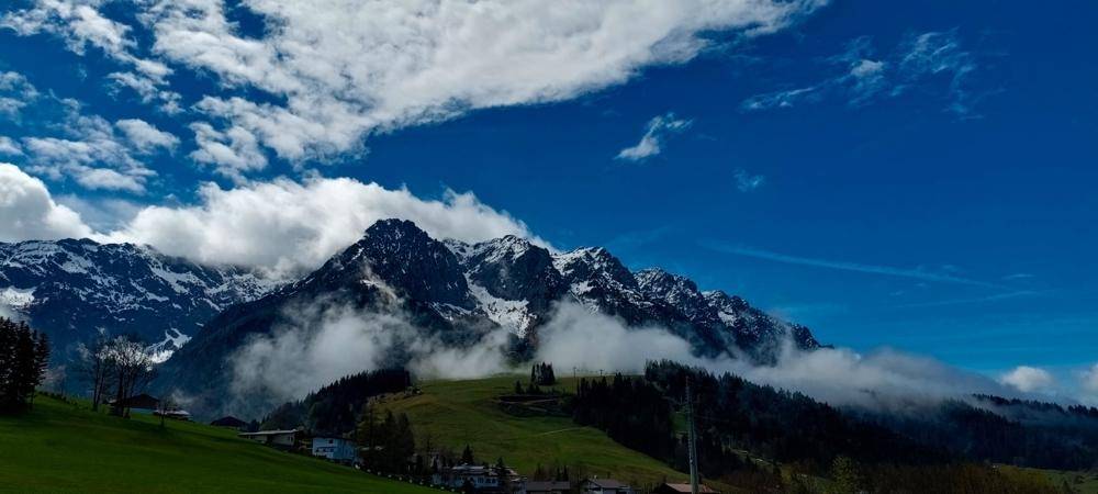 Dramatischer Blick auf die Bergwelt mit Wolken, die die Gipfel umhüllen, unter blauem Himmel.