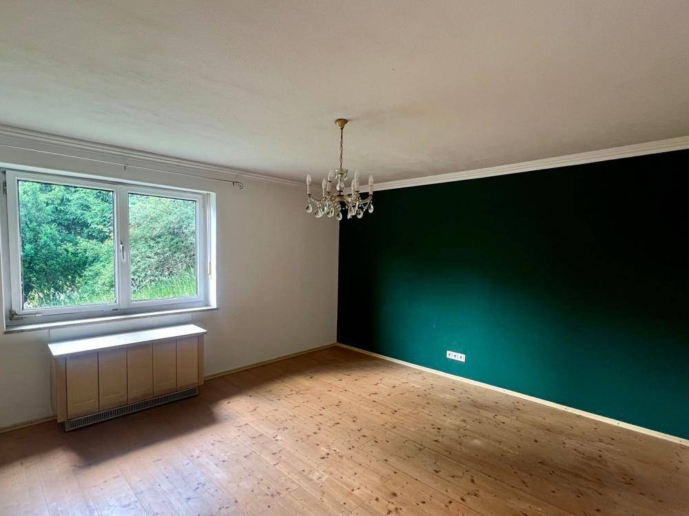 Schlafzimmer mit Holzboden, grüner Akzentwand und einem klassischen Kronleuchter.