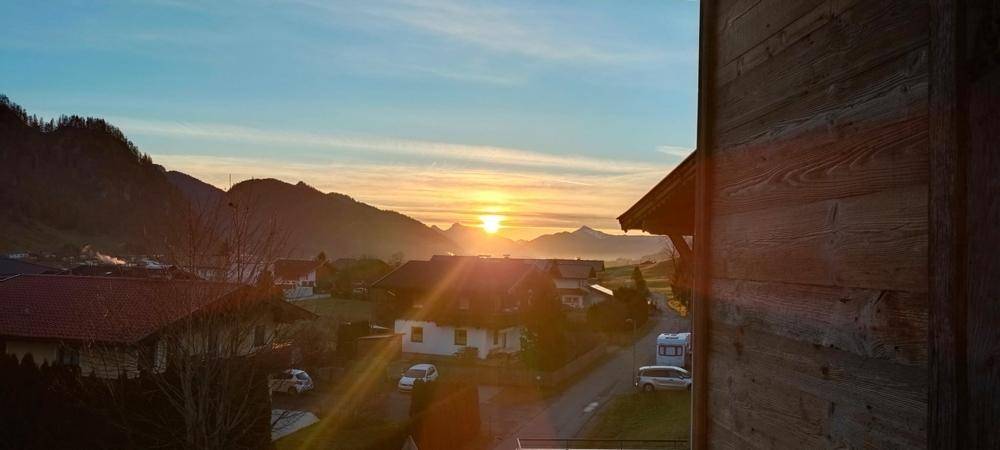 Spektakulärer Sonnenuntergang über der ländlichen Umgebung mit Häusern und Bergen im Hintergrund.