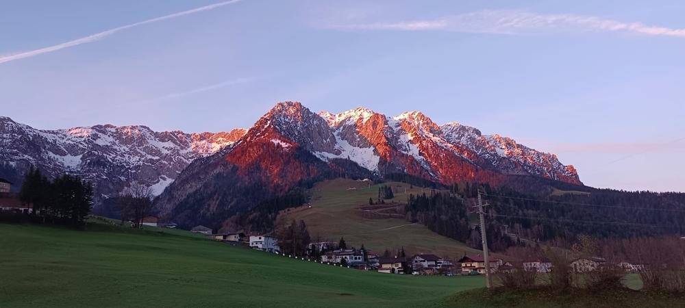 Atemberaubender Sonnenuntergang über den schneebedeckten Berggipfeln, die in warmen Farben leuchten.